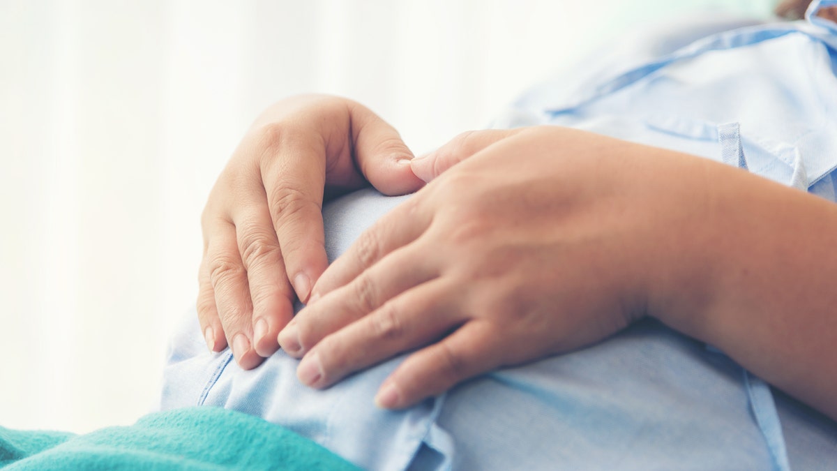 Pregnant woman holds belly from hospital bed