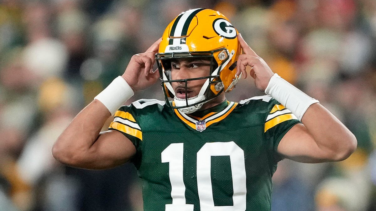 Jordan Love of the Green Bay Packers with both hands raised above his head, placed on his helmet.