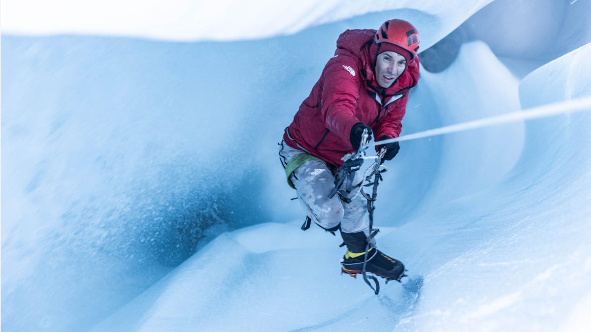 A man, Alex Honnold, rappels down a blue-white glacier hole carved by water.
