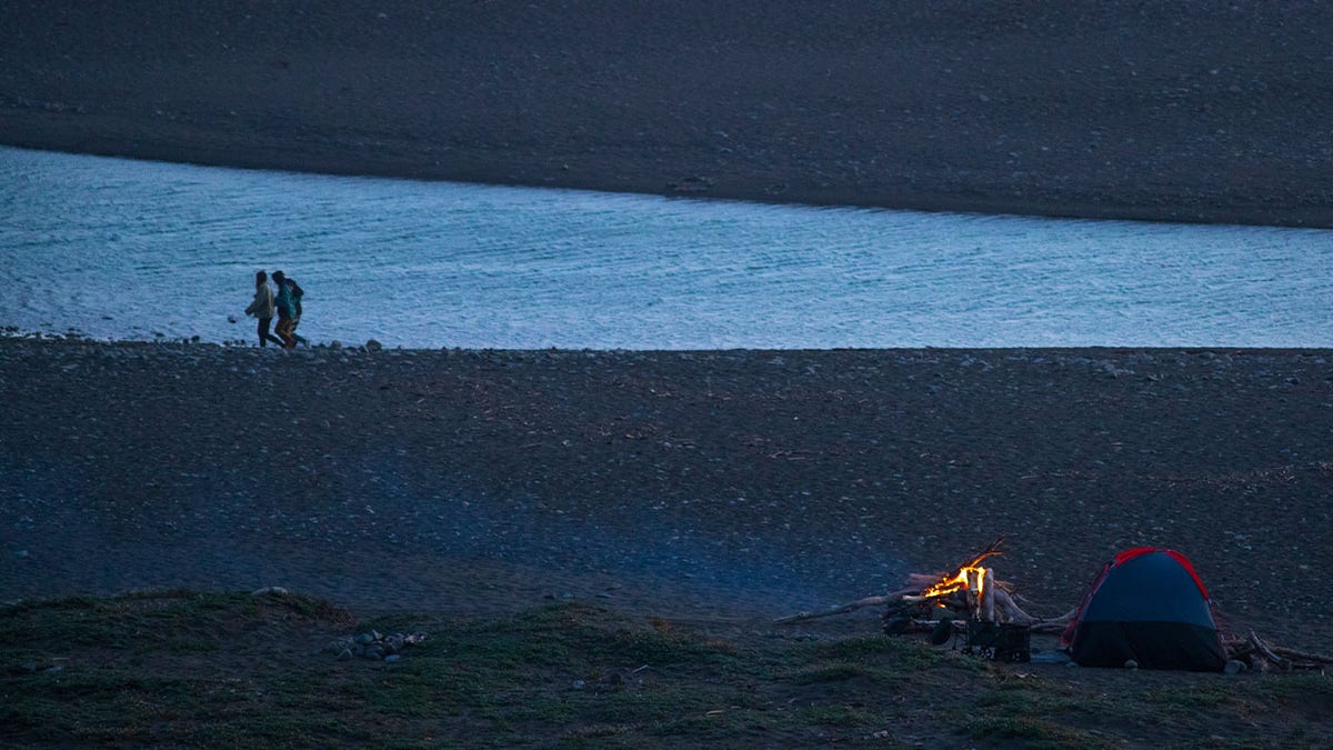 Beachgoers walk along the shore as a campfire glows on the beach at San Carpoforo Creek on California Highway 1 near Ragged Point on Saturday, May 1, 2021 in Big Sur, CA.