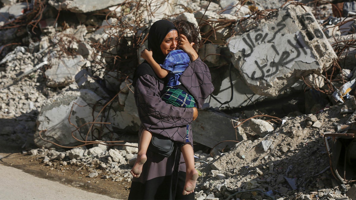 A Palestinian woman carrying her child in her arms cries in front of a collapsed building as the dead bodies of Palestinians who died in Israel's attack on the Bureij Refugee Camp are brought to the al-Awda Hospital for burial in Gaza City, Gaza on Sept. 19, 2024.