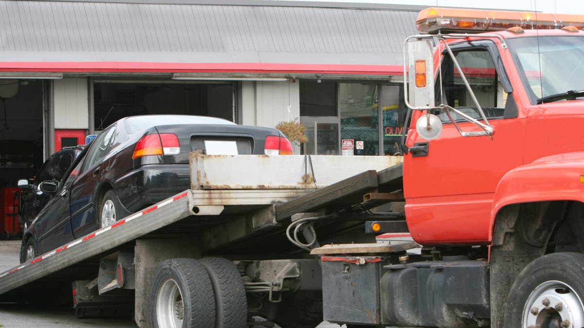 A tow truck brings a car to a repair shop.