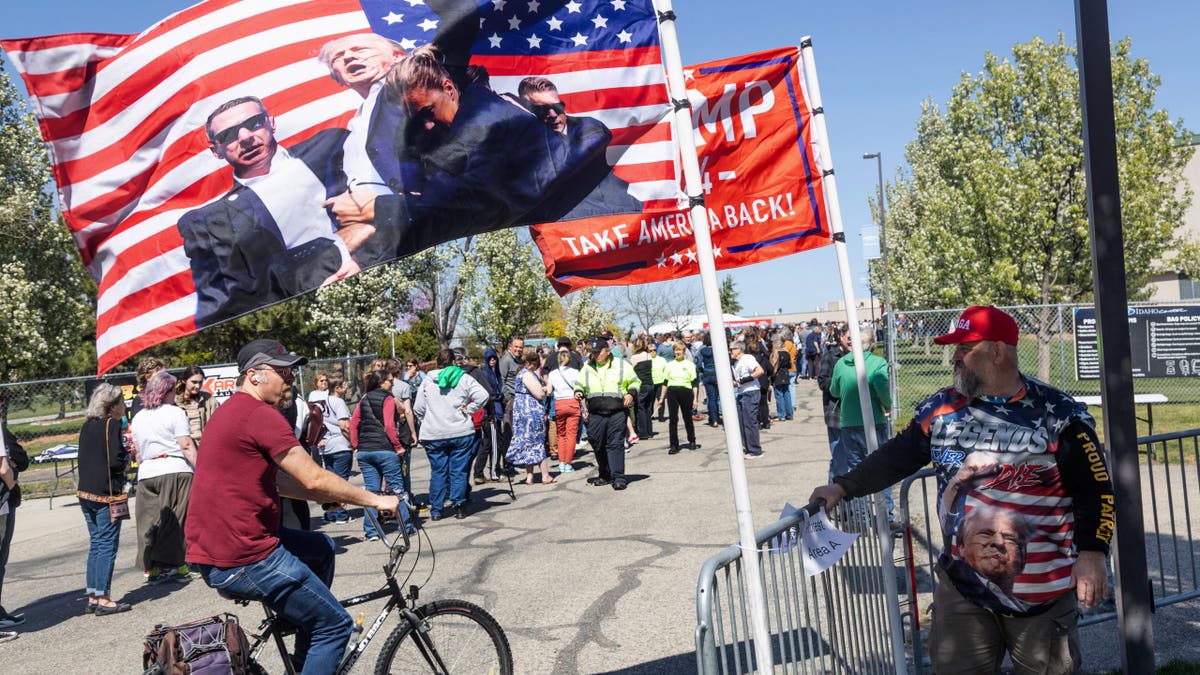 Michael Thompson stands by a pair of Trump flags as attendees line up to enter the "Fighting Oligarchy" event at the Ford Idaho Center in Nampa, Idaho, on April 14, 2025.