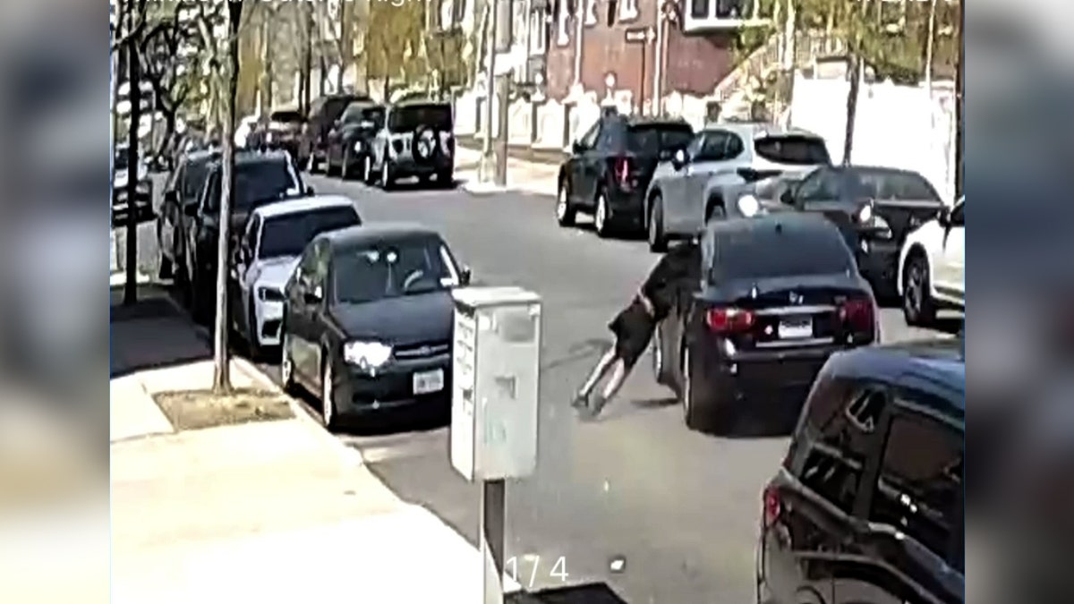 man hanging outside car window as car drives through street
