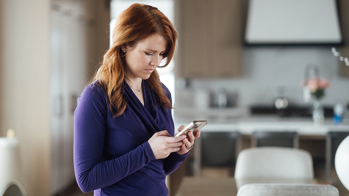 Elizabeth Smart wearing a purple sweater and looking down at a phone.