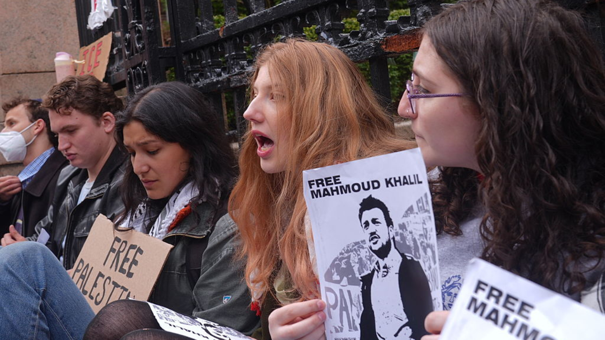 Students chained to gate at Columbia University hold up a paper that says "Free Mahmoud Khalil"