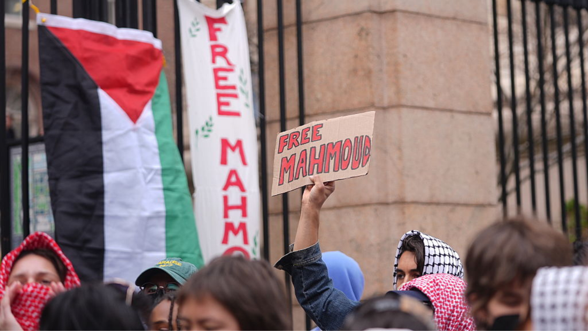 A woman can be seen holding up a cardboard sign that says 'Free Mahomoud'