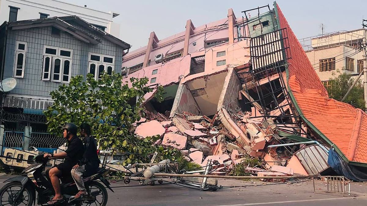 People drive on a motorbike past a collapsed building in Mandalay 
