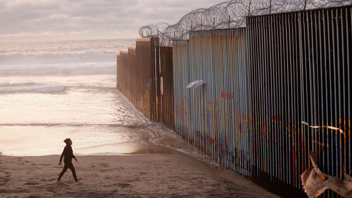 A woman walks on the beach next to the border wall topped with razor wire in Tijuana, Mexico.