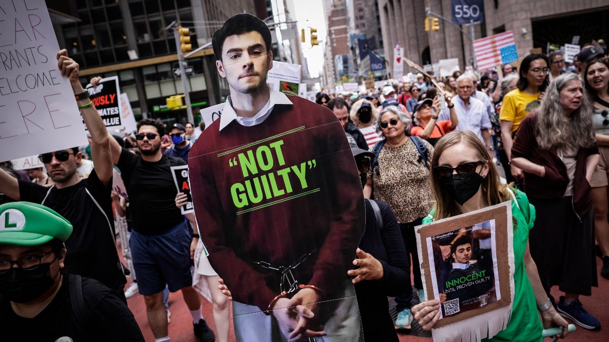A woman carries a poster with the image of Luigi Mangione as people hold up signs during a rally titled "Protect Migrants, Protect the Planet," in New York City on April 19, 2024.