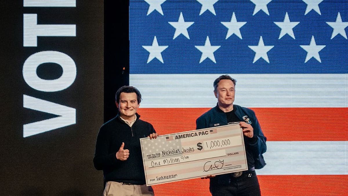 Elon Musk, chief executive officer of Tesla Inc., right, presents a one million dollar check to an attendee during an America PAC town hall ahead of the Wisconsin Supreme Court election at the KI Convention Center in Green Bay, Wisconsin, US, on Sunday, March 30, 2025. Musk's plan to hand out $1 million checks to two residents for participating in Wisconsin's Supreme Court election is barred by state law, a new complaint said Friday. Photographer: Jamie Kelter Davis/Bloomberg via Getty Images
