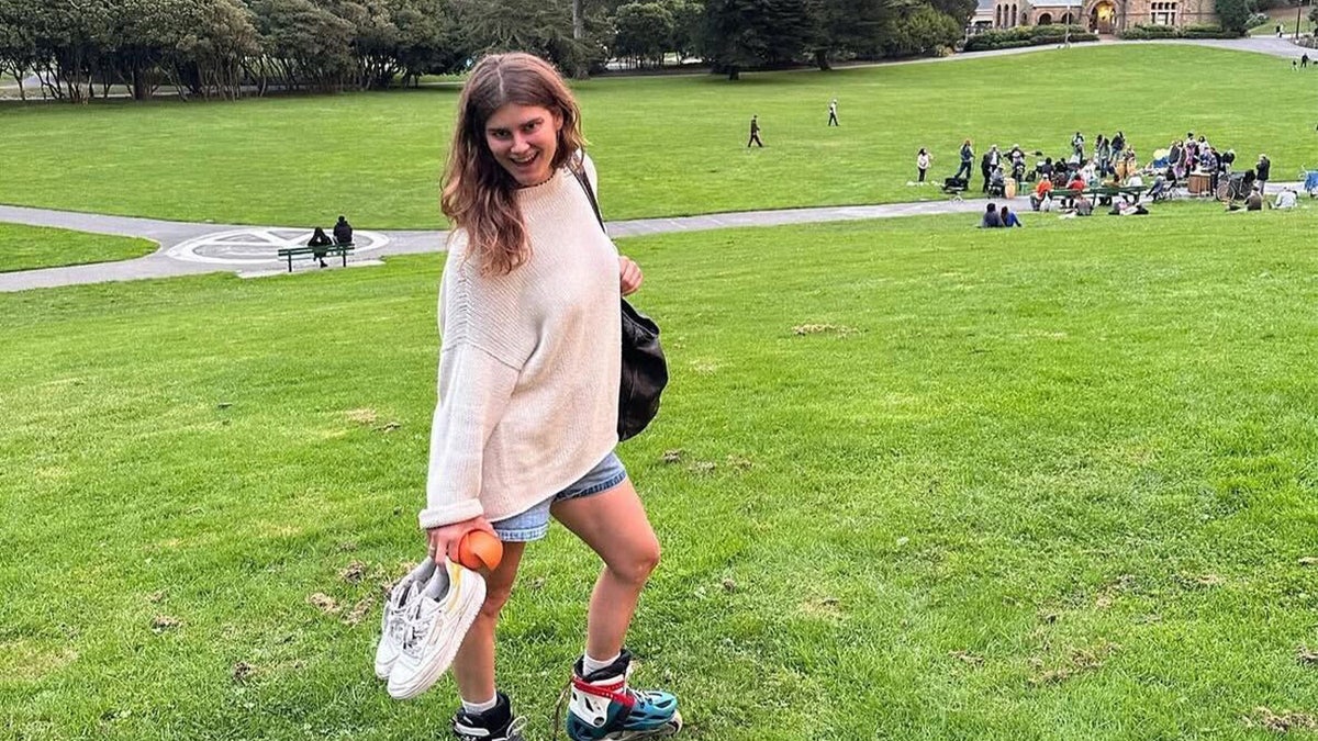 Ellery Curtis, wearing a white sweater and jean shorts, stands in lawn