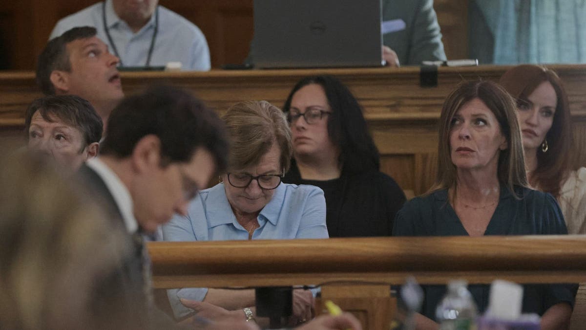 Peggy O'Keefe, wearing a baby blue shirt and glasses, lowers her head during testimony about her son's murder