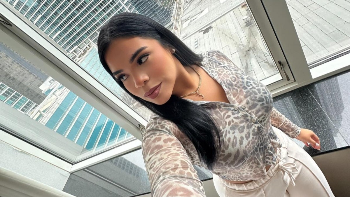Jennifer Contreras takes a selfie in front of a window showing high-rise buildings