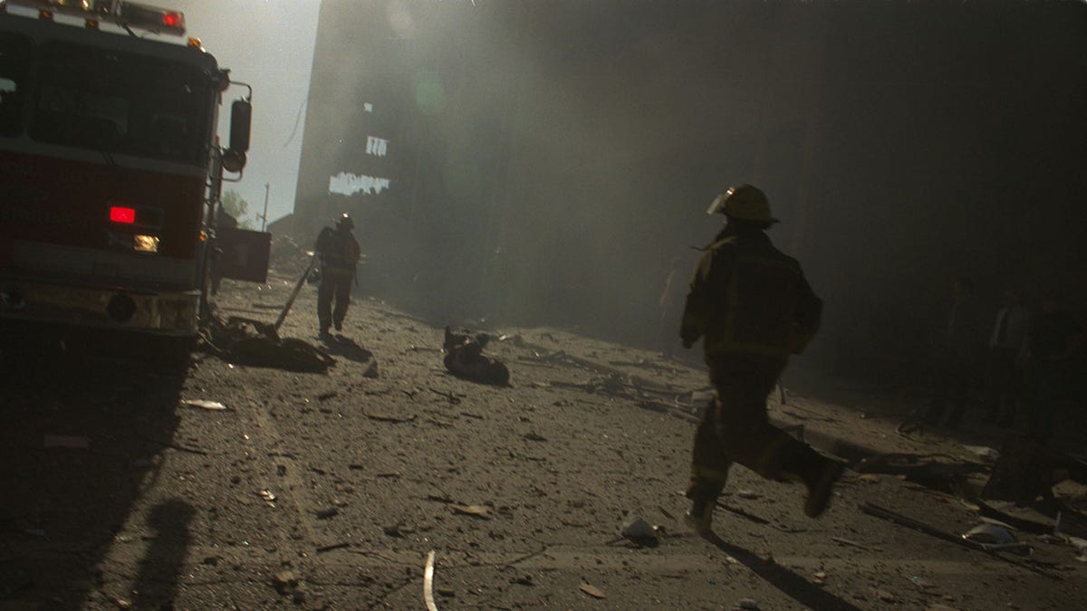 Firefighters running through thick smoke and debris.
