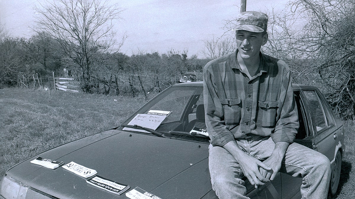 A black and white photo of Timothy McVeigh sitting on bonnet of his car.