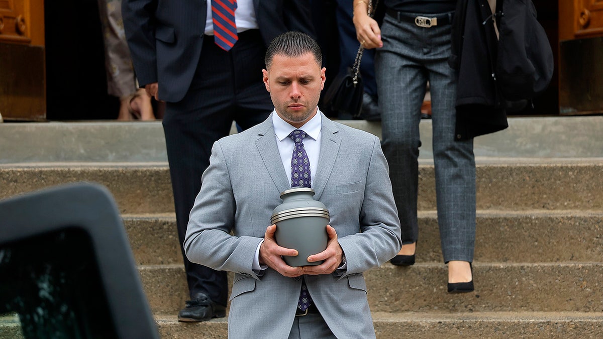 A man in a grey suit holding Nathan Carman's cremains.