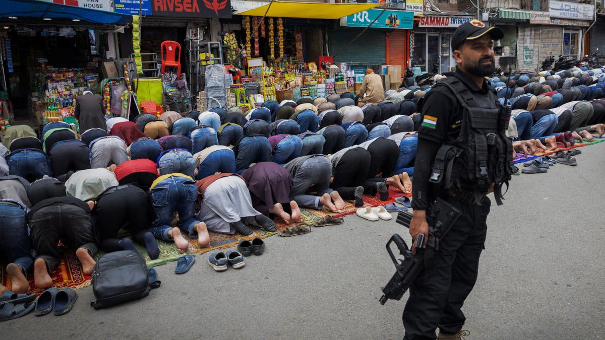 Kashmiri Muslims offering Friday prayers while Indian security guard stands watch