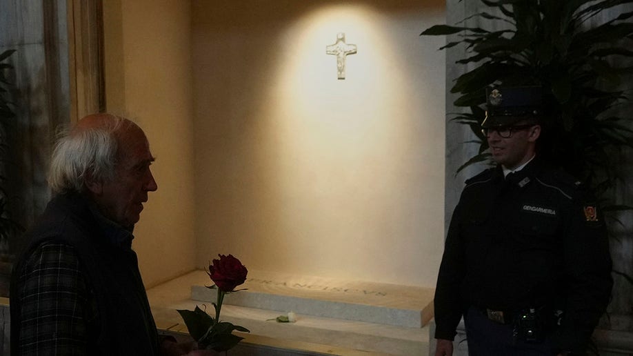 A mourner holds a red rose in front of the tomb of Pope Francis