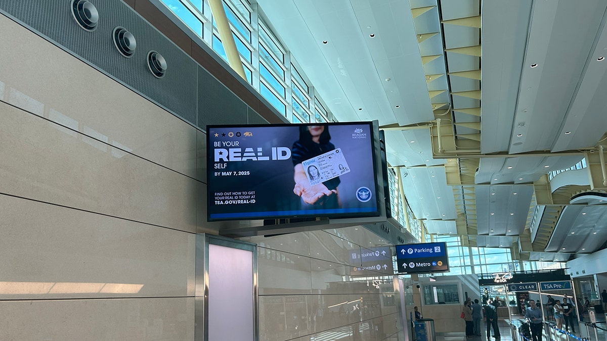 A display on a TV at an airport of a woman holding out her "REAL ID" to encourage travelers to get their REAL ID done before the travel ban takes place.
