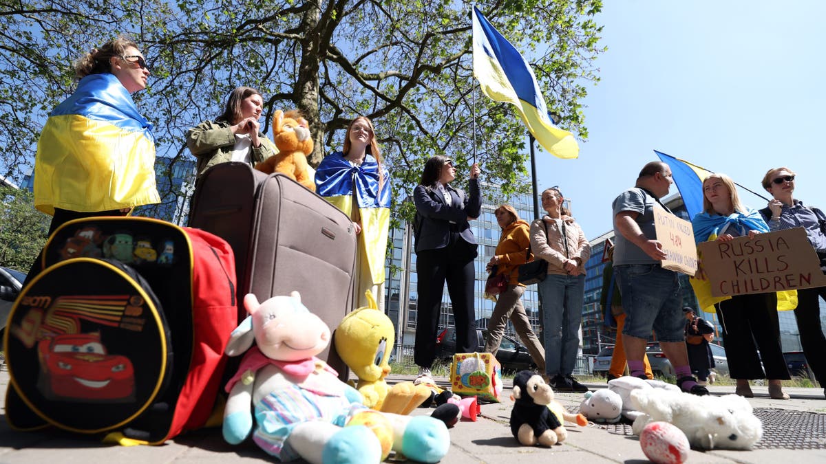 People, holding banners and Ukrainian flags, gather to demonstrate for the extradition of Ukrainian children abducted by Russia in front of the United Nations office in Brussels.