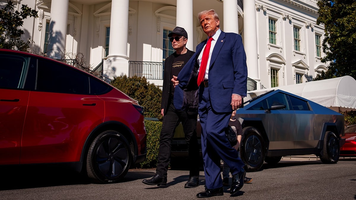 Donald Trump and Elon Musk walk by a red Tesla vehicle parked outside the White House