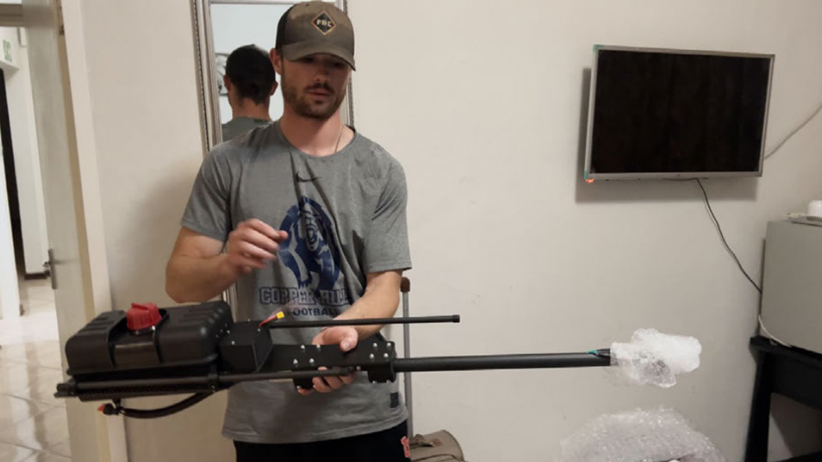 Thompson unpacks the flamethrower drone  attachment from its box and displays it for the camera.