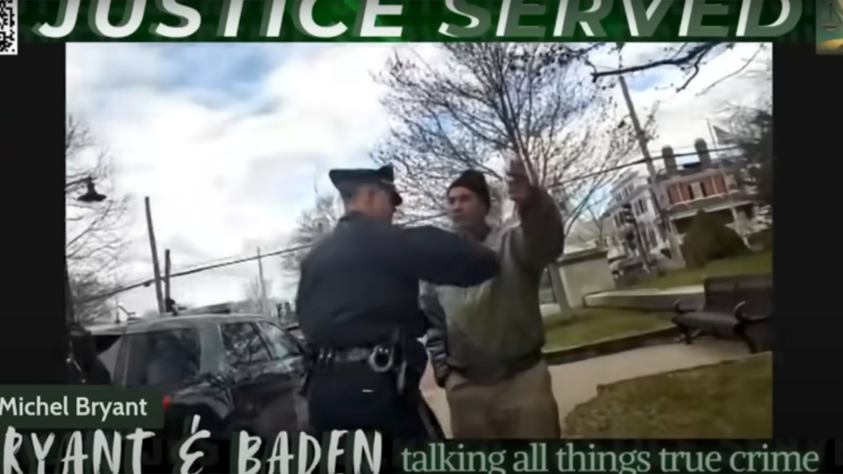 A uniformed police officer has his hand on the chest of a man in a green jacket