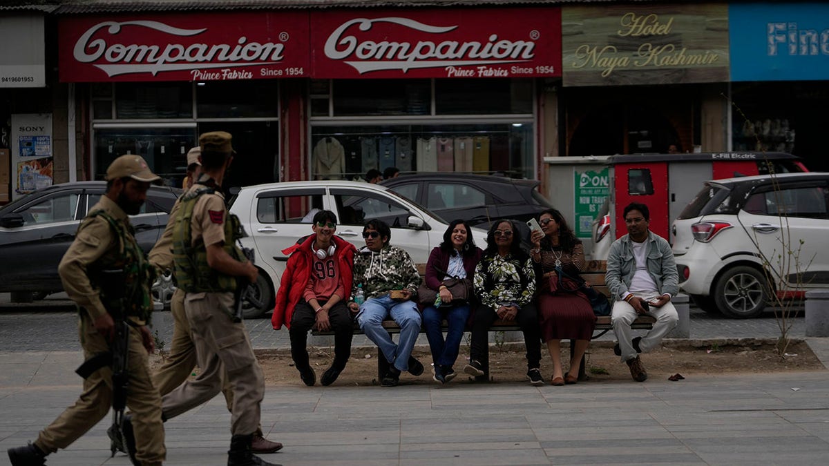 Indian tourists rest on a bench as policemen pass by
