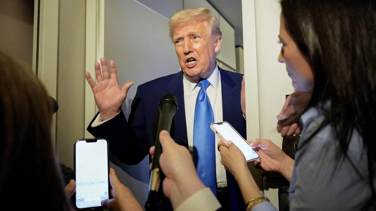 Donald Trump in blue tie talking to reporters on Air Force One