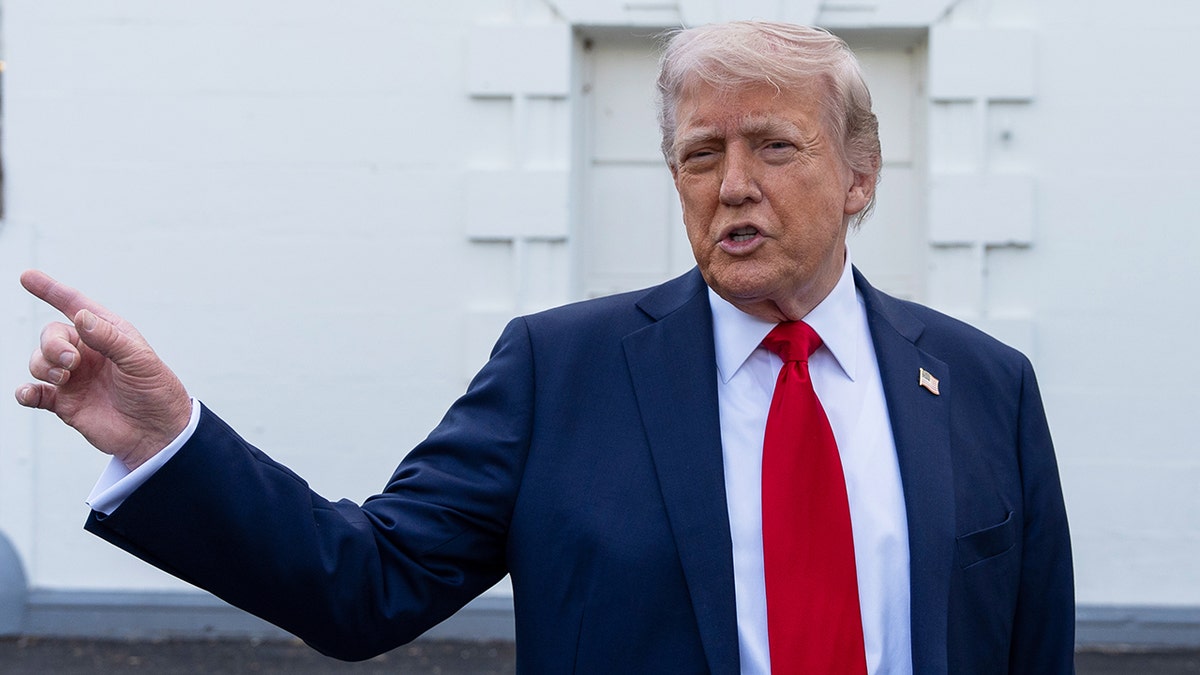 Trump in a red tie pointing while speaking with reporters outside White House