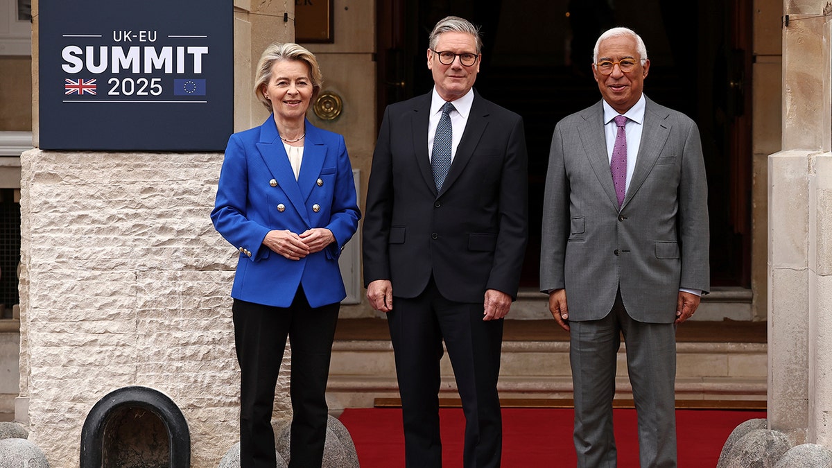 U.K. Prime Minister Keir Starmer stands between European Commission President Ursula von der Leyen and European Council President António Costa outside Lancaster House in London during the UK–EU Summit 2025, with a summit sign visible on the wall beside them. All three leaders pose on a red carpet in front of the entrance.