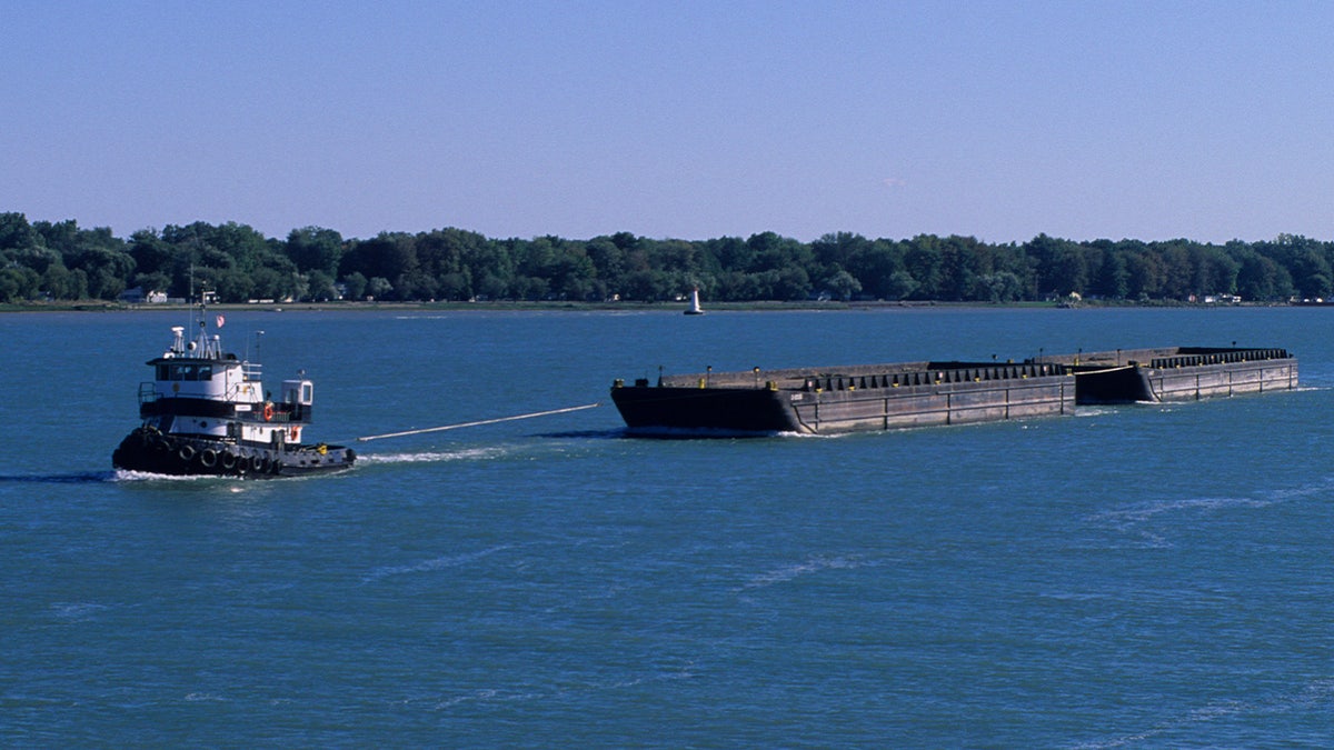 A tugboat pulls a barge along the U.S-Canada border