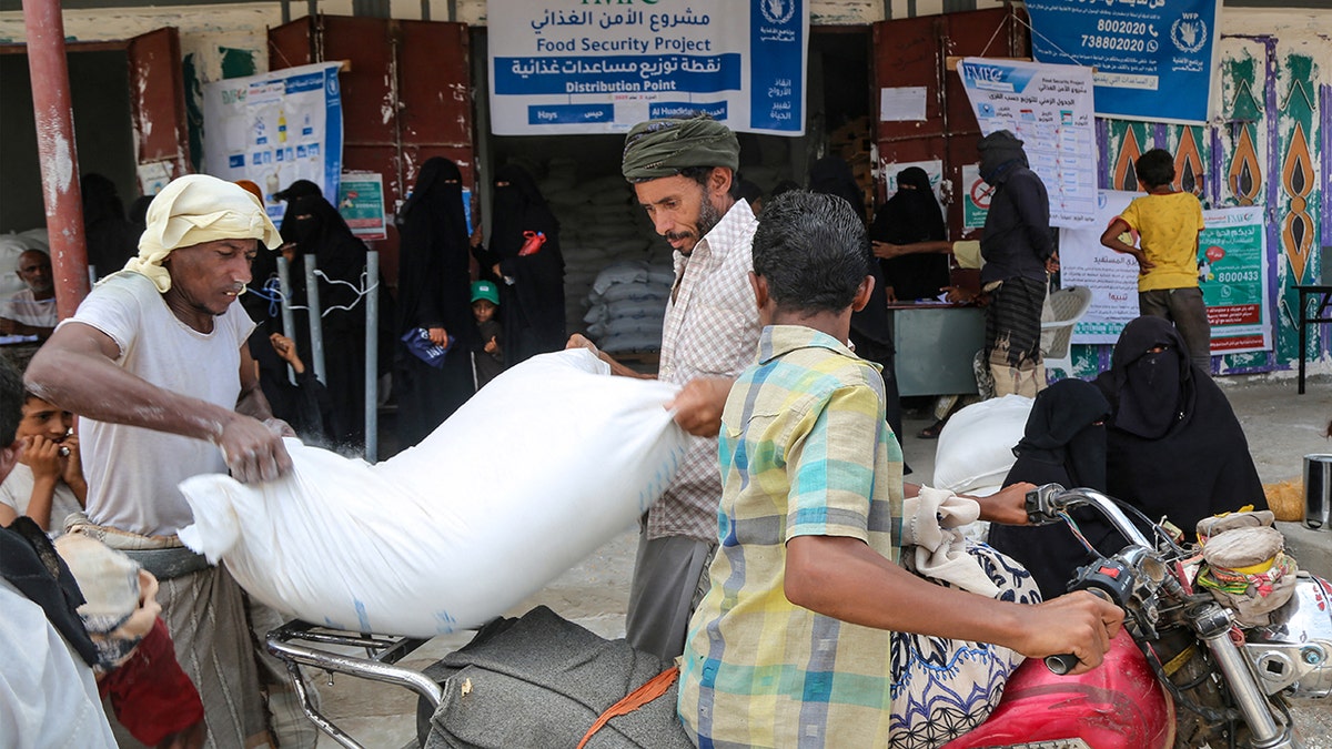 Yemeni men load food supplies with women fully covered in black veils mind children