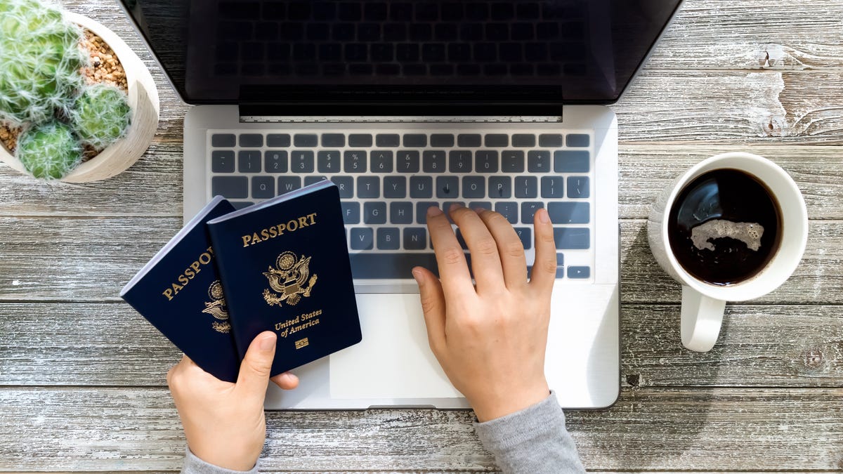 A person holds two American passports while typing on a laptop computer