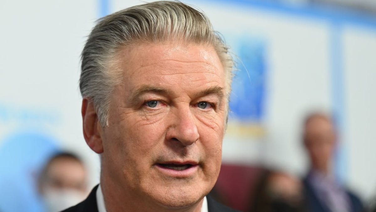 Actor Alec Baldwin looks at the camera, with white and blue standee in the background, in a 2021 shot