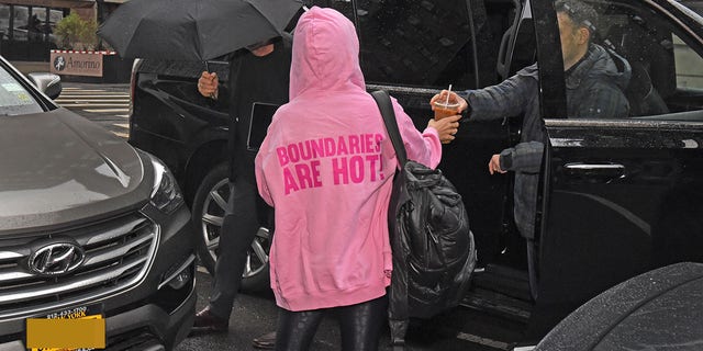 Hilaria Baldwin arrives at home with Alec Baldwin wearing a pink hoodie with "boundaries are hot!" across the back.