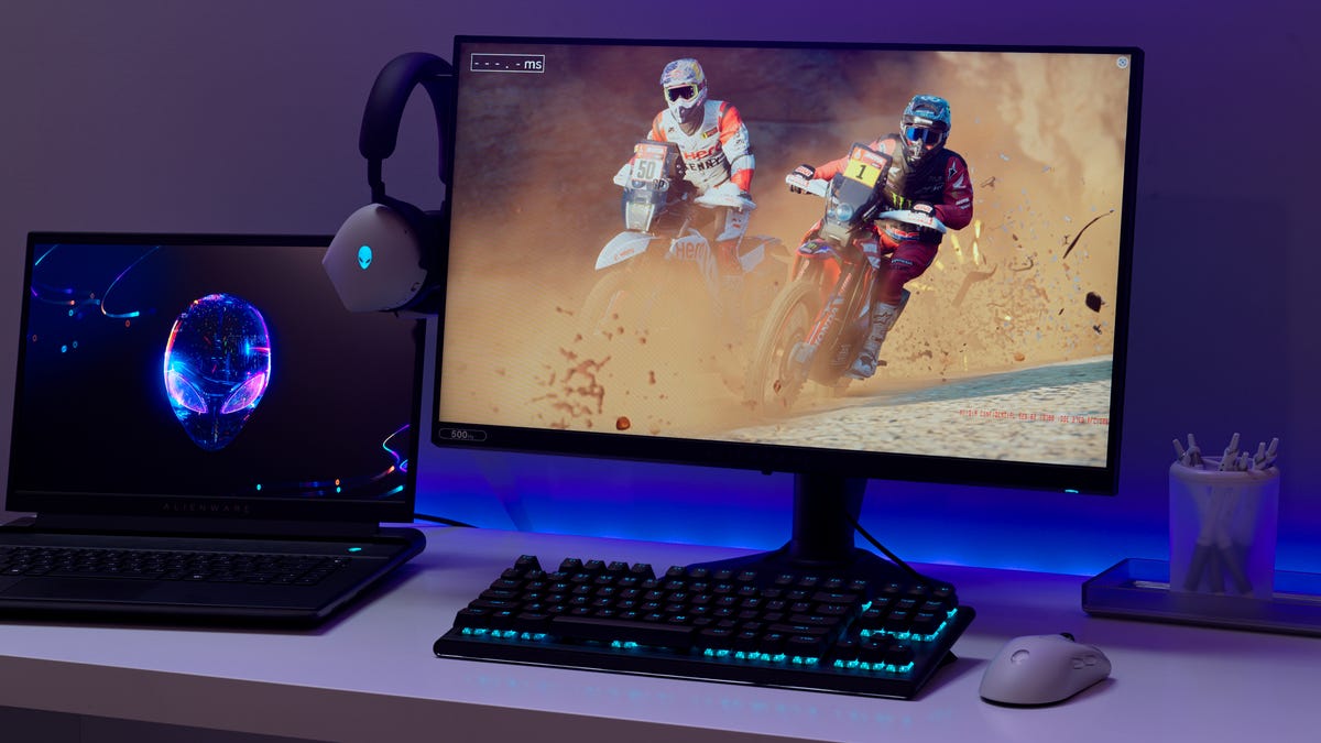 The Alienware 500Hz gaming monitor connected to a laptop, surrounded by Alienware accessories and showing motorcyclists on the screen