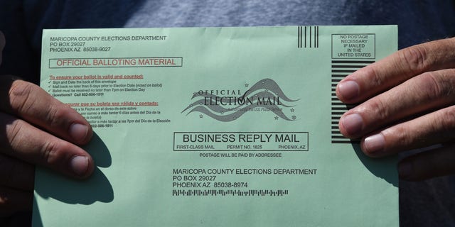 A voter displays their mail-in ballot envelope as they arrive to cast their ballot in the U.S. presidential election at an early voting location in Phoenix on Oct. 16, 2020.