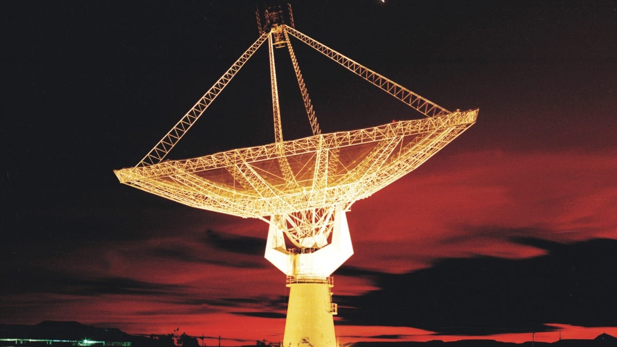 A large satellite dish is pointed toward a reddish sky during what appears to be late sunset.