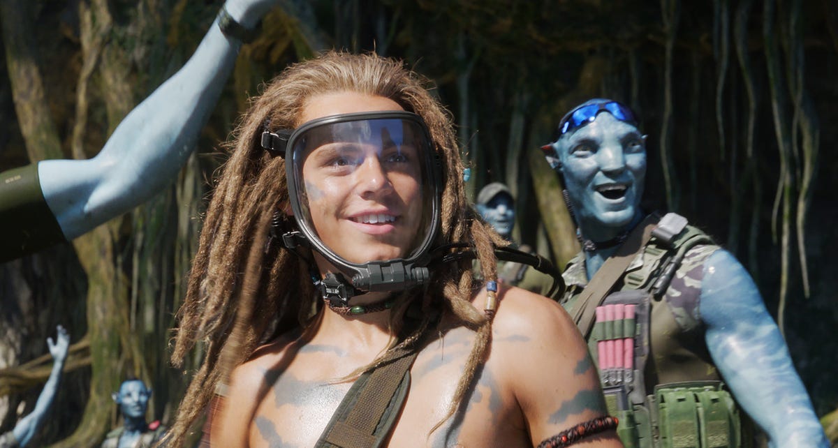 A young man grins in a breathing mask surrounded by blue aliens in sci-fi sequel Avatar: The Way of Water.