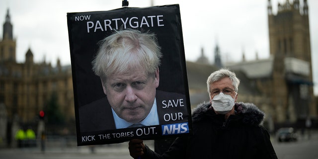An anti-Conservative Party protester holds a placard with an image of British Prime Minister Boris Johnson by Parliament, in London, Dec. 8, 2021.