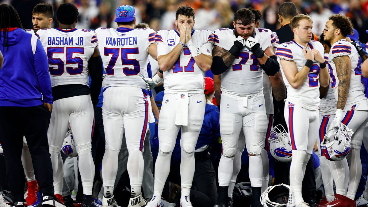 Buffalo Bills Quarterback Josh Allen faces the camera with his hands over his face in front of other Buffalo Bills players.