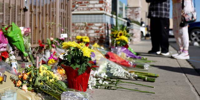 People stand at a makeshift memorial outside the scene of a deadly mass shooting at a ballroom dance studio in Monterey Park, California. An eleventh person has died and ten more were injured at the studio near a Lunar New Year celebration on Saturday night. 