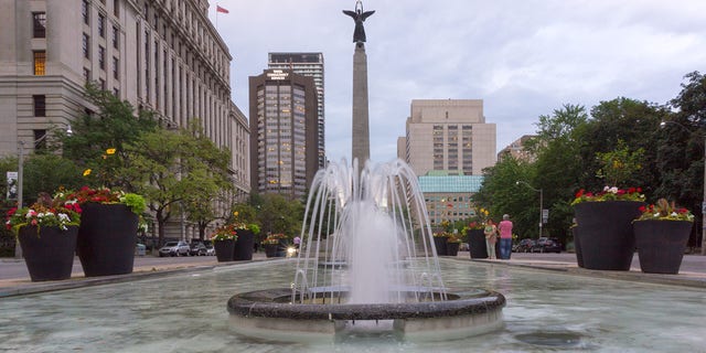 This file image shows a fountain in the downtown district of Toronto. The famous place is in a city square with large pots and commercial buildings around. 