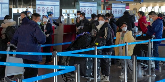Masked travelers with luggage line up at the international flight check in counter at the Beijing Capital International Airport in Beijing, Thursday, Dec. 29, 2022. Moves by the U.S., Japan and others to mandate COVID-19 tests for passengers arriving from China reflect global concern that new variants could emerge in its ongoing explosive outbreak — and the government may not inform the rest of the world quickly enough. 