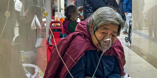 An elderly patient receives an intravenous drip while using a ventilator in the hallway of a Beijing hospital on Jan. 5, 2023.
