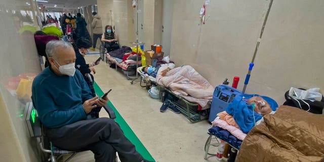 People wearing face masks browse their phones and look on as their elderly relatives receive intravenous drips in a Beijing hospital corridor on Jan. 5, 2023.