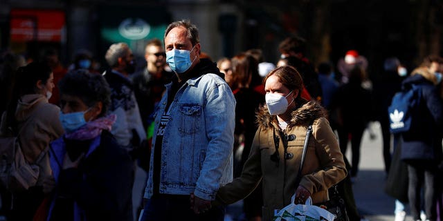 People wear protective face masks as they walk down a street in Madrid, Spain, on Feb. 7, 2022.