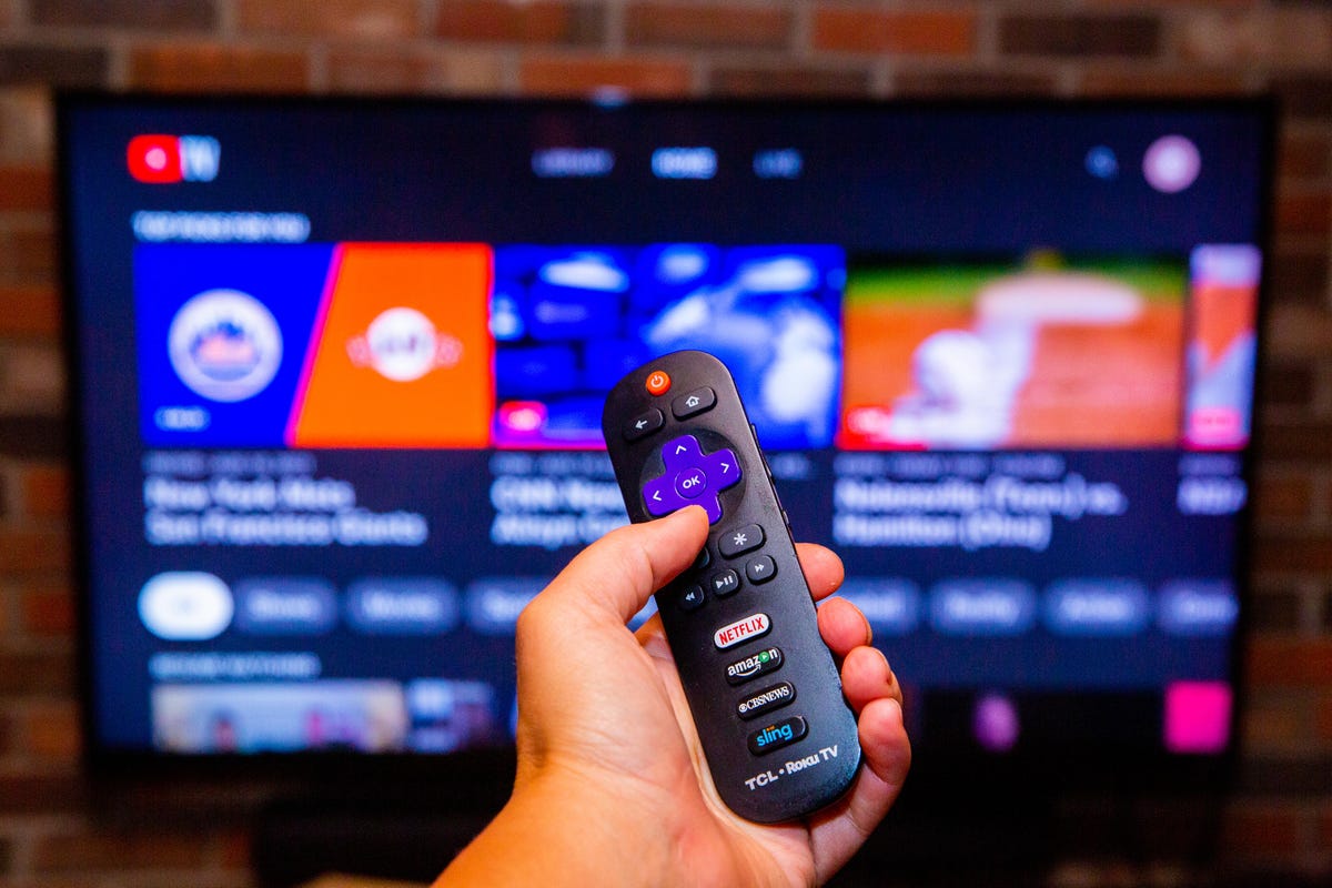 Youtube TV on a screen, with a hand holding a remote control in the foreground